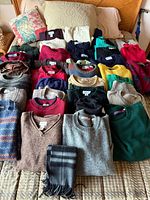 All sweaters and scarf laid out on bed