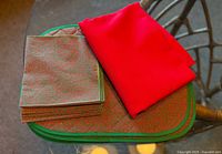 Stack of placemats with green trim, napkins on top, red runner folded