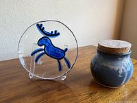 Front view of Bergdala glass plate beside ceramic jar