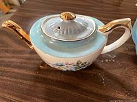 Gibsons teapot left profile showing spout, lid, blue band, floral motif and gold trim