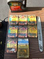 Overall view of bar oil, six Oregon chain packages, Blue Hawk chain pack, loose chain case, and guide bar