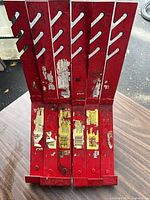 Six red Qual-Craft 2500 adjustable roofing brackets stacked upright showing slotted adjustment arms and worn labels