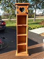 full view of tall narrow wooden cabinet with open shelves and heart cutout door