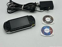 Front view of PSP console, power adapter, two UMD discs