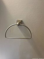 Front view of wall-mounted brushed nickel hand towel holder with semicircular bar and square backplate