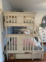 Front view showing cream wood bunk bed, ladder, rails, mattresses, trundle front panel