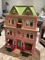 Front view of pink three-story dollhouse with green roof