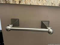 Front view of brushed nickel toilet paper holder mounted to wall showing full bar and both brackets