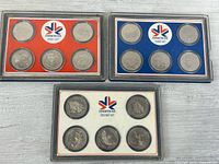 Three coin sets in display cases showing colour inserts and coin arrangement