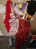 Clown jumpsuit draped over table with red feather boa and black curly wig visible