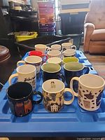 Front angled view of 22 assorted ceramic mugs on blue tray