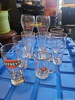 Group of assorted beer glasses on blue tote showing all branded and plain pieces