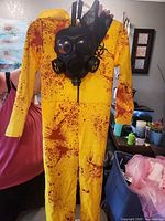 Full view yellow splatter jumpsuit held upright with gas mask positioned at chest