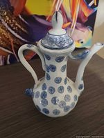 Front view of porcelain ewer teapot with lid displaying blue shou symbols and lotus detail