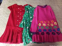 Three casual knit dresses in red, green and fuchsia laid flat