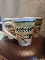 Three mugs displayed showing olive branch artwork and rim band