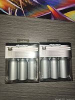 Front view of two sealed Tracker travel bottle sets showing three silver bottles per set