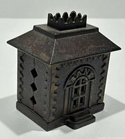 Three-quarter view of cast iron building-form bank showing roof finial and saw-tooth sides