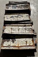 Stack of distressed tin ceiling tiles showing floral pattern and chippy white paint