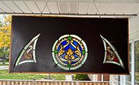 Full view of wood panel with three stained glass inserts hanging outdoors