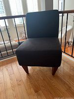 Front view of dark grey armless chair showing upholstery and legs