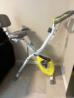 Side view of folded white and yellow exercise bike showing seat, handlebars, flywheel cover