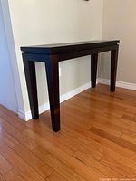 Full view of dark wooden side table against wall, showing top, legs, and floor for scale