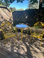 Overall view of two yellow wrought iron chairs and matching glass-top table on deck