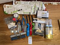 Overview of entire lot on floor showing power strips, thermostat, aerosol cans, lighters, tools, hardware and packaging