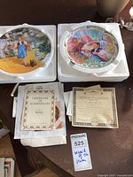 Two Wizard of Oz plates in Styrofoam holders, both Certificates of Authenticity visible