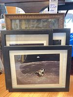 Stacked framed prints: three black-framed NASA Apollo 11 prints in front, ornate wood-framed cathedral print behind