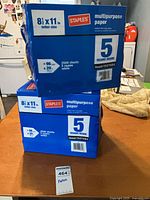 Two blue Staples multipurpose paper cartons stacked on table