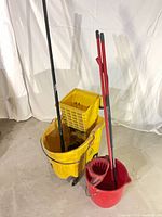 Yellow commercial bucket with attached wringer and black handle, red household bucket with red handles