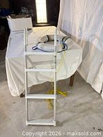 Pool ladder leaning against table with life ring and rope visible