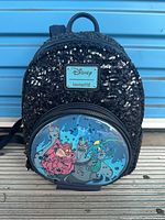 Front view of black sequin mini backpack with Disney Loungefly plaque and printed Muses front pocket