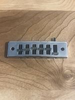 Front view of chrome rectangular six-saddle guitar bridge showing saddle slots and intonation screws