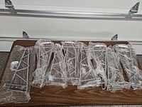 Eight chrome shelf brackets in plastic sleeves on table