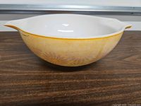 Side view of bowl showing faded orange color, daisy pattern, rim chip and handle.