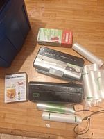 Two vacuum sealers, two boxed rolls, six loose bag rolls displayed on floor