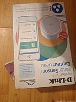 Front of boxed D-Link mydlink Wi-Fi Water Sensor, visible device image, crushed lower corner