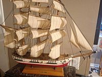 Overall front and side view of model ship on stand showing sails and hull