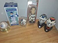 Group shot of all items showing bobblehead box, autographed baseball, Devils ball in cube, NHL figure, two goalie masks