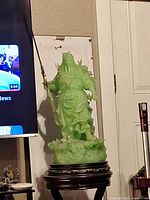 Full view of green warrior statue on wooden stand beside TV for scale