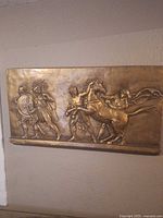Full view of rectangular bronze-tone bas relief plaque on wall