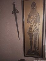 Framed knight print and sword mounted on wall