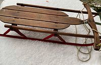 Side view of full wooden sled on snow showing red runners and deck