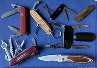 All seven pocket knives and multi-tools laid out on blue background
