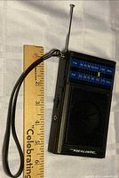 Front view showing radio size relative to ruler, wrist strap, antenna extended