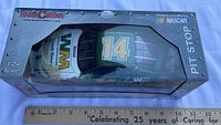 Factory-sealed Team Caliber Pit Stop 1:24 scale die-cast car #14 Waste Management in retail box beside ruler for scale