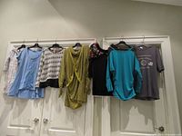 Seven tops hung on hangers displayed against wall